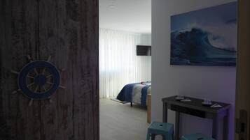 Una habitación con cama, escritorio, silla, televisor y un cuadro de una ola.