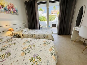 A hotel room with two beds, a desk, a chair, and a view of the outside. - Americas Holiday Home (Playa de las Américas)
