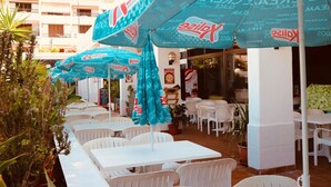 Espace extérieur aménagé avec des tables et des chaises blanches, protégé par des parasols bleus arborant le logo « Kalis ».