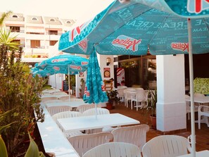 Outdoor seating with white tables and chairs, covered by blue umbrellas with 'Kalis' branding.