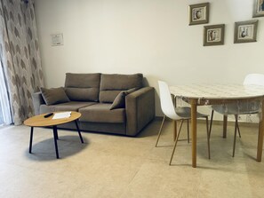 A living room with a sofa, a coffee table, a dining table with chairs, and a wall with framed pictures. - Americas Holiday Home (Playa de las Américas)
