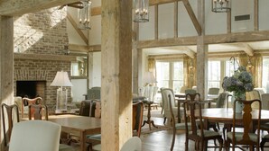 A spacious dining area with wooden tables and chairs, a brick fireplace, and large windows allowing natural light. - Ballast Point Bungalow - Waterfront Harmony (Oriental)