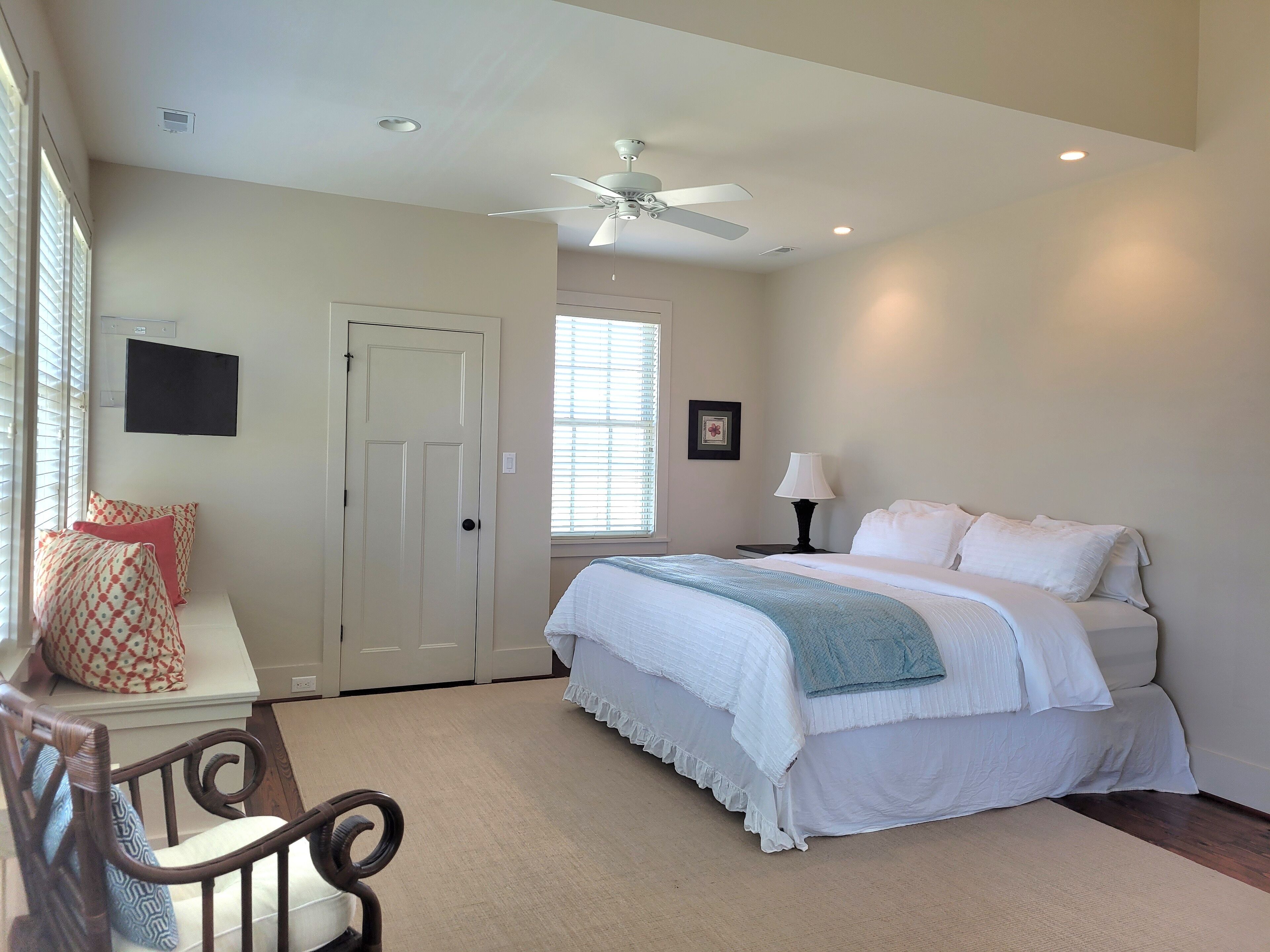 A bedroom with a bed, a desk with a chair, a ceiling fan, and a window with blinds.