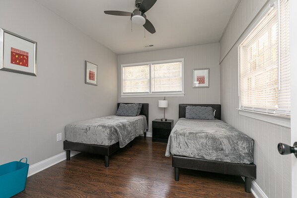 A bedroom with two beds, a ceiling fan, a window with blinds, and a blue chair.