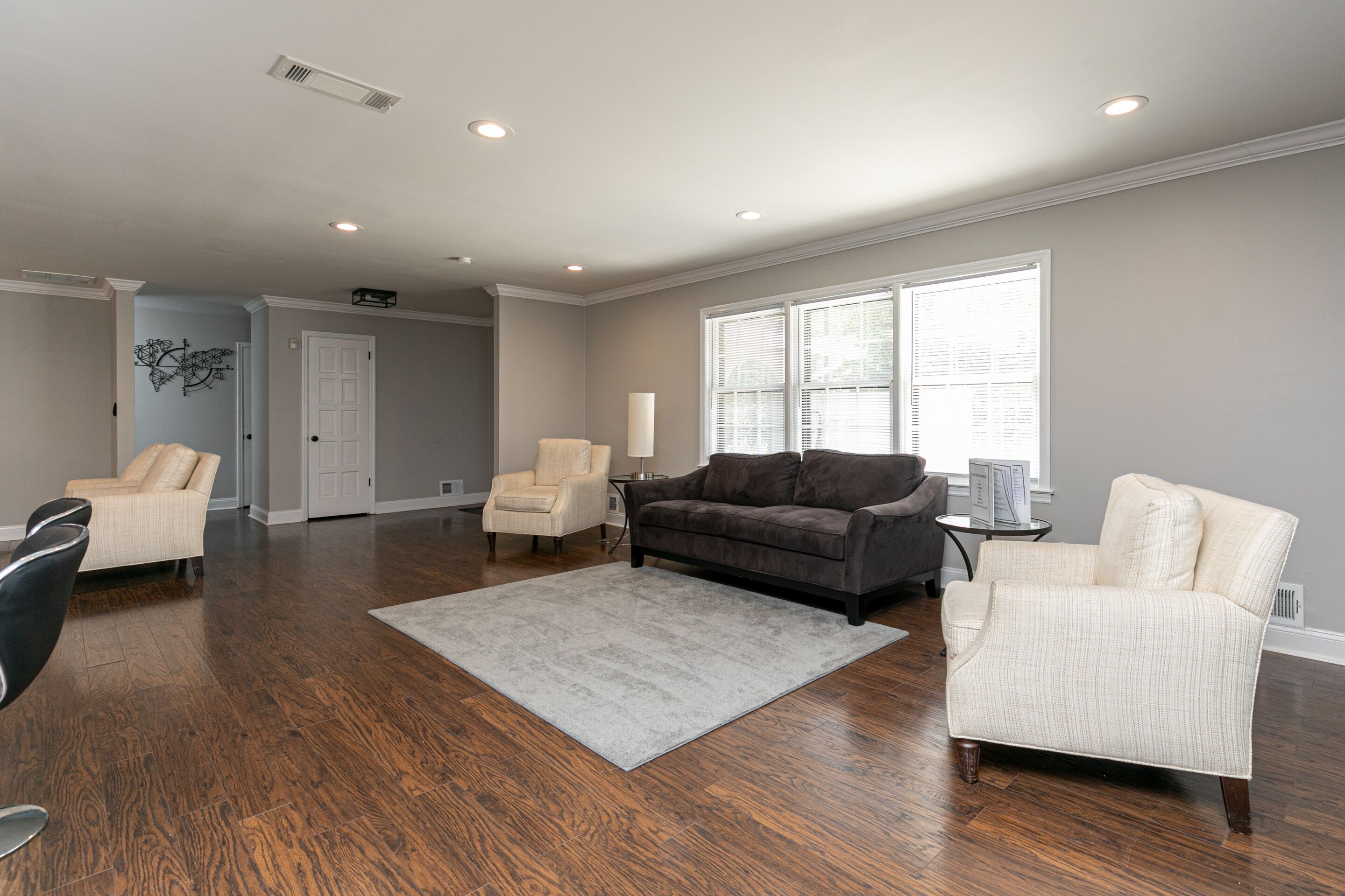 A spacious living room with hardwood floors, a gray rug, and two armchairs.