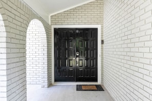Uma porta dupla preta com moldura branca, embutida numa parede de tijolos brancos com um arco.