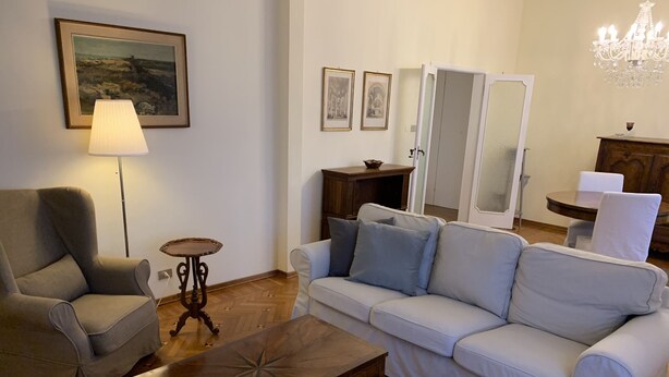 Uma sala de estar com sofá, poltrona, mesa de centro, abajur e lustre.