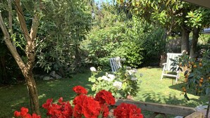 Um jardim com um banco de madeira, uma árvore e flores vermelhas.