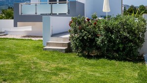 A modern two-story house with a glass balcony, a white umbrella, and a well-maintained lawn.