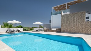 A modern outdoor swimming pool with lounge chairs and umbrellas, surrounded by a stone wall and a glass balustrade.