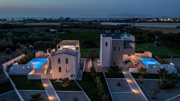 A modern villa with a swimming pool, a covered patio, and a view of the sea.