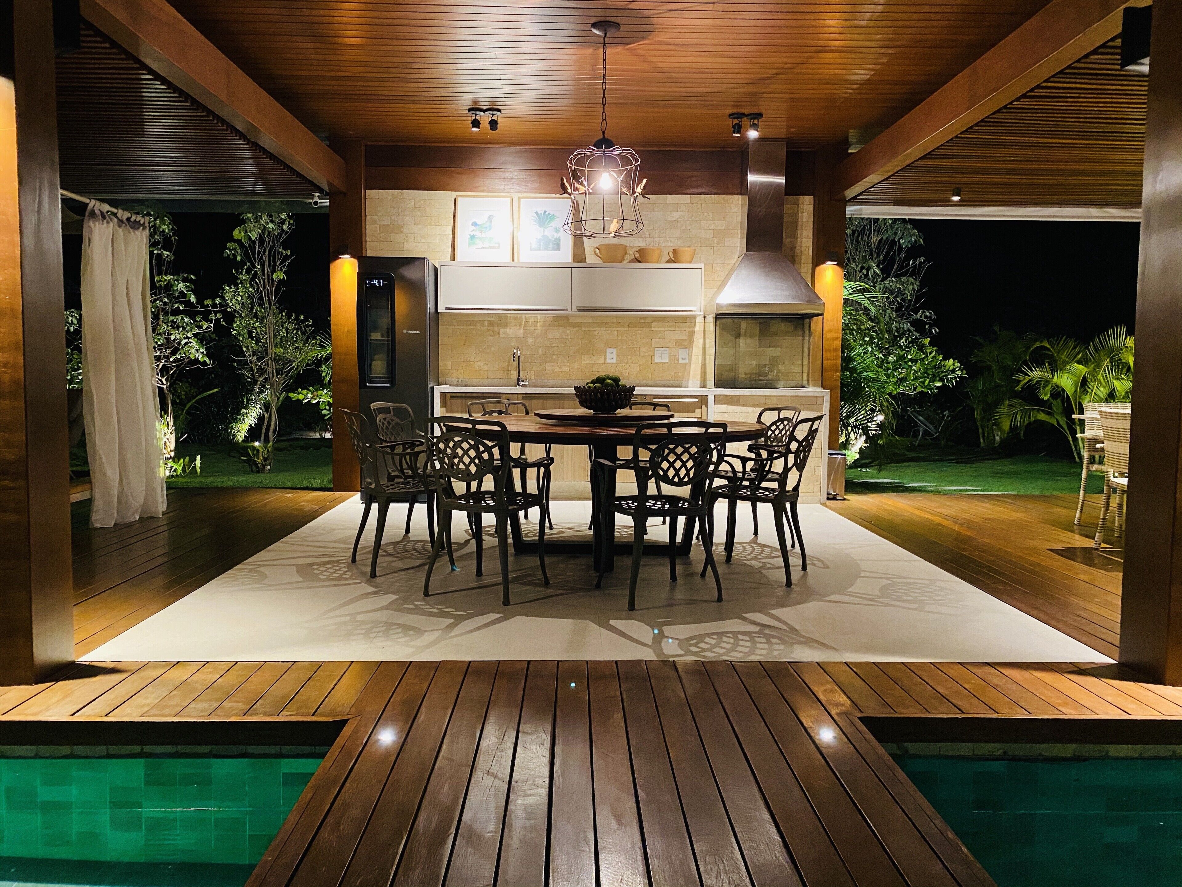 An outdoor dining area with a pool, wooden deck, and a modern kitchen with a large island.