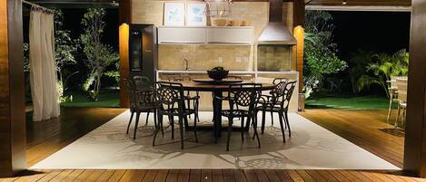 An outdoor dining area with a pool, wooden deck, and a modern kitchen with a large island.