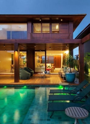 Uma casa moderna de dois andares com um deck de madeira e uma piscina.