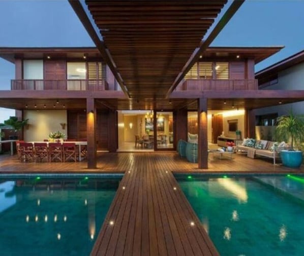 Uma casa moderna de dois andares com um deck de madeira que dá para uma piscina.
