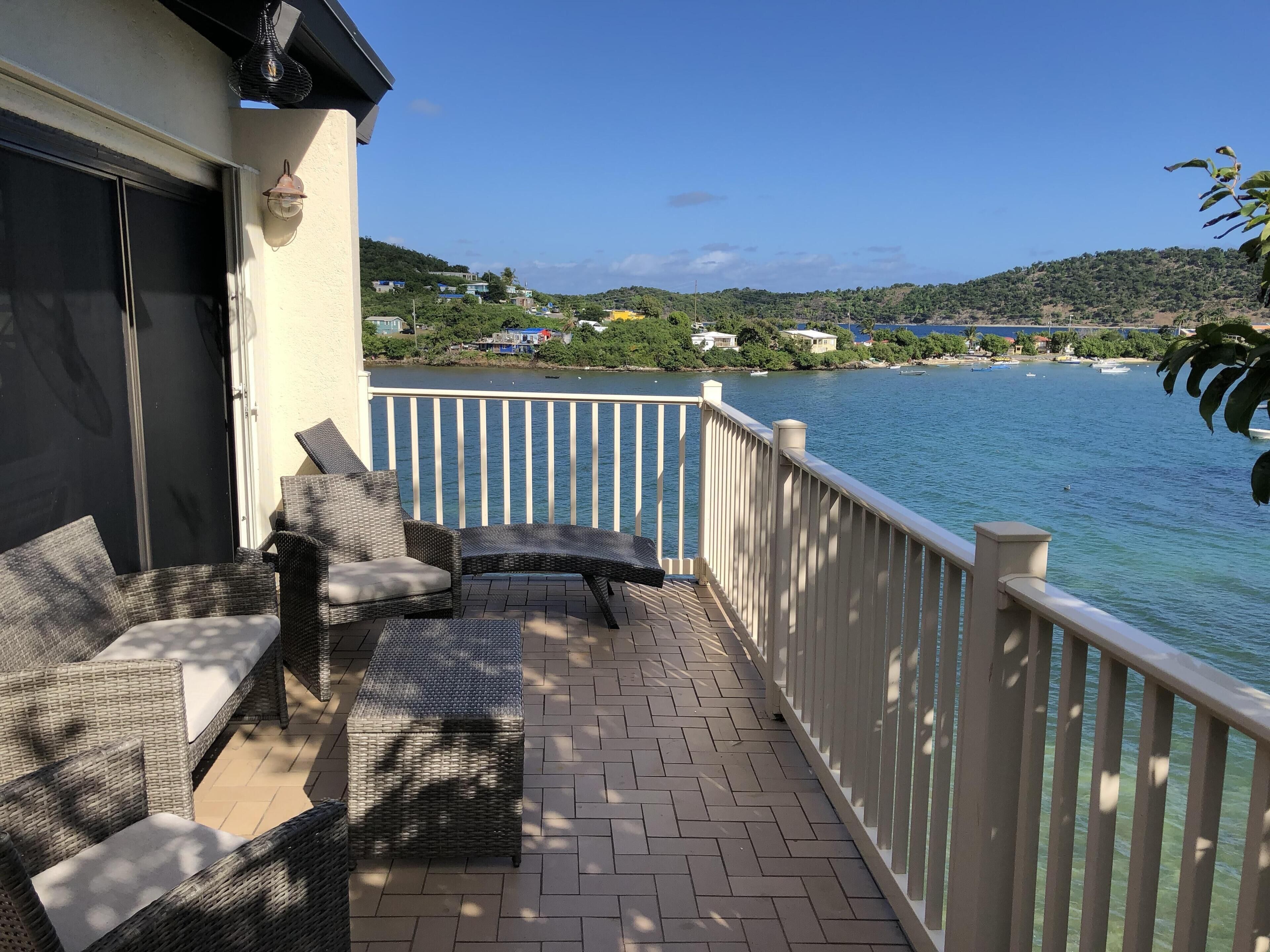 Un balcon agrémenté de meubles en osier, avec vue sur un lac et des maisons en arrière-plan.