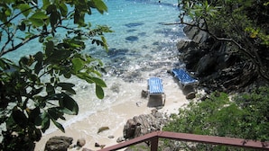 A beach with clear water, two striped beach chairs, and rocky terrain.