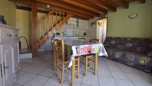 Un comedor con una mesa y sillas de madera, un sofá y una cocina al fondo.