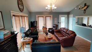 A living room with a fireplace, leather sofas, a chandelier, and a bookshelf. - Viewtopia - New Hot Tub with Amazing Views on 160+ acres (Rock Spring)