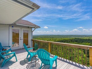 Une terrasse avec des chaises turquoise et une table, d’où l’on peut admirer un paysage boisé.