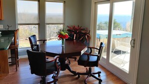 A dining area with a wooden table, four chairs, a vase with flowers, and a view of the outdoors through large windows. - Viewtopia - New Hot Tub with Amazing Views on 160+ acres (Rock Spring)