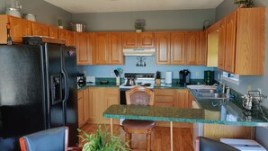 A kitchen with wooden cabinets, a black refrigerator, a stove, and a dining area with chairs and a table. - Viewtopia - New Hot Tub with Amazing Views on 160+ acres (Rock Spring)