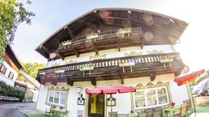 A traditional chalet-style building with a balcony, outdoor seating area, and a green awning. - Inntalhof Pension (Raubling)