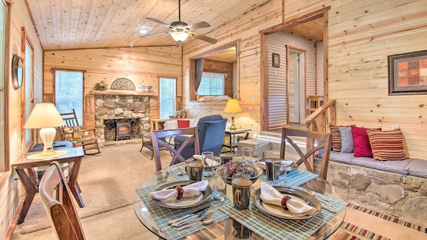 A cozy log cabin interior with a dining area, stone fireplace, and comfortable seating. - Updated Cabin w/ Porch, Mins to Cossatot River (Wickes)