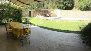 Eine Terrasse mit rundem Tisch und Stühlen, einer Steinmauer und einem Pool im Hintergrund.