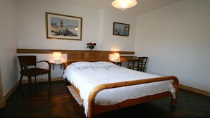 A bedroom with a wooden bed, two chairs, a nightstand with a lamp, and two framed pictures on the wall.