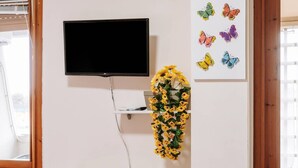 A room with a flat-screen TV mounted on the wall, a shelf with decorative items, and a table with a bowl and a glass.
