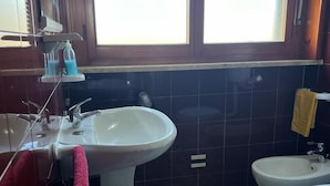 A bathroom with a pedestal sink, a toilet, a bidet, and a window with blinds.