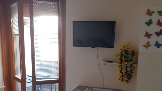 A room with a sliding glass door leading to a balcony, a flat-screen TV mounted on the wall, a grey dresser, and a wall-mounted air conditioning unit.