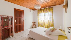 Ein Schlafzimmer mit Holzboden, einem Bett mit weißer Bettwäsche, einem Holzschrank und einem Fenster mit blumigen Vorhängen.