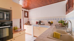 Eine kompakte Küche mit Mikrowelle, Backofen und Spüle. Eine kleine Kücheninsel beherbergt einen Wasserkocher und eine Kaffeemaschine. Die Küche verfügt über eine geflieste Spritzwand und eine Holzzahlende.