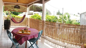 Eine überdachte Terrasse mit Tisch für zwei Personen, einer Hängematte und Blick auf Grünflächen und Gebäude.