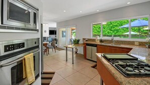 Et moderne køkken med rustfrie stålapparater, et spiseområde med bord og stole, og udsigt til grøn vegetation udenfor.