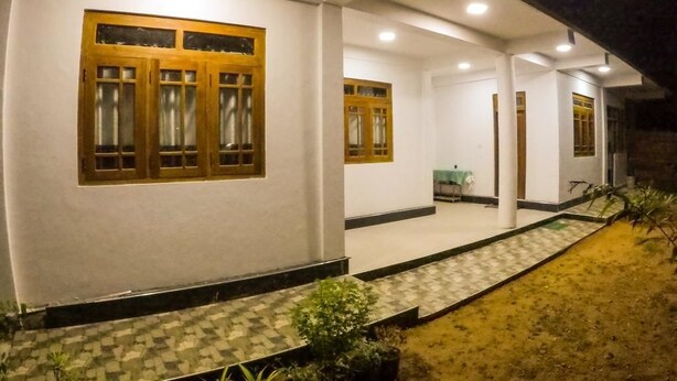 A building with a covered porch, multiple windows with wooden frames, and a tiled walkway leading to the entrance. - Sunwon Holiday Home (Dambulla)