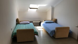 Una habitación pequeña y luminosa con dos camas individuales, una mesa y un banco.