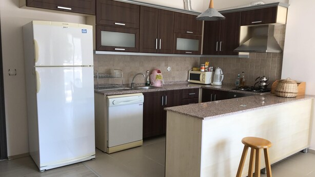 Una cocina con armarios de madera oscura, un refrigerador blanco, un microondas, una estufa y un taburete de madera.