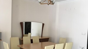 Un comedor con una mesa redonda, seis sillas, una araña y un espejo grande en la pared.