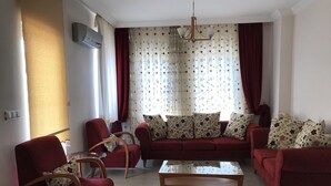 Una sala de estar con un sofá rojo, una mesa de centro de madera y cortinas decoradas.