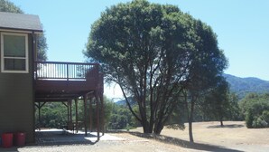 A covered outdoor area with a wooden deck, a large tree, and a building with a window. - Luxury Lake Suite  9 Hole & Disc Golf with Hot Tub, Views, Large Patios. (Dos Rios)