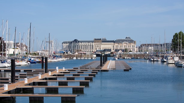 Un port de plaisance avec de nombreuses jetées et des bateaux, un grand bâtiment en arrière-plan et une eau calme.