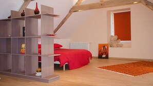 Ein Schlafzimmer mit schrägen Wänden, einem roten Bett, einem Holzregal, einem Teddybären und einer Heizung.
