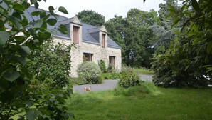 Ein steinerner Winkel mit geneigtem Dach, umgeben von üppigem Grün und einem kleinen Hund im Garten.