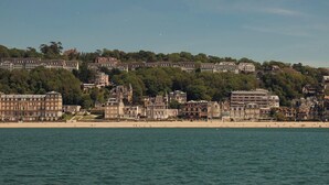 Un pueblo costero con playa, edificios históricos y una colina con construcciones residenciales.