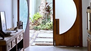 Un acceso con un amplio recorte circular que da a un jardín con un árbol y plantas.