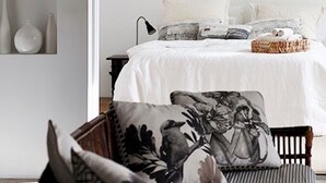 Un dormitorio con cama, almohadas, mesita de noche, lámpara y ventana.
