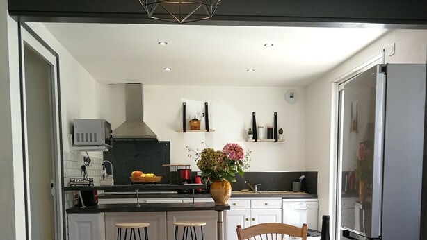 A modern kitchen with a dining area. The kitchen features a black and white checkered floor, a central island with a vase of flowers, and a hanging light fixture. The dining area has a round table with chairs and a chandelier. - Apartment completely renovated in ground floor. (Saint-Jean-Pied-de-Port)